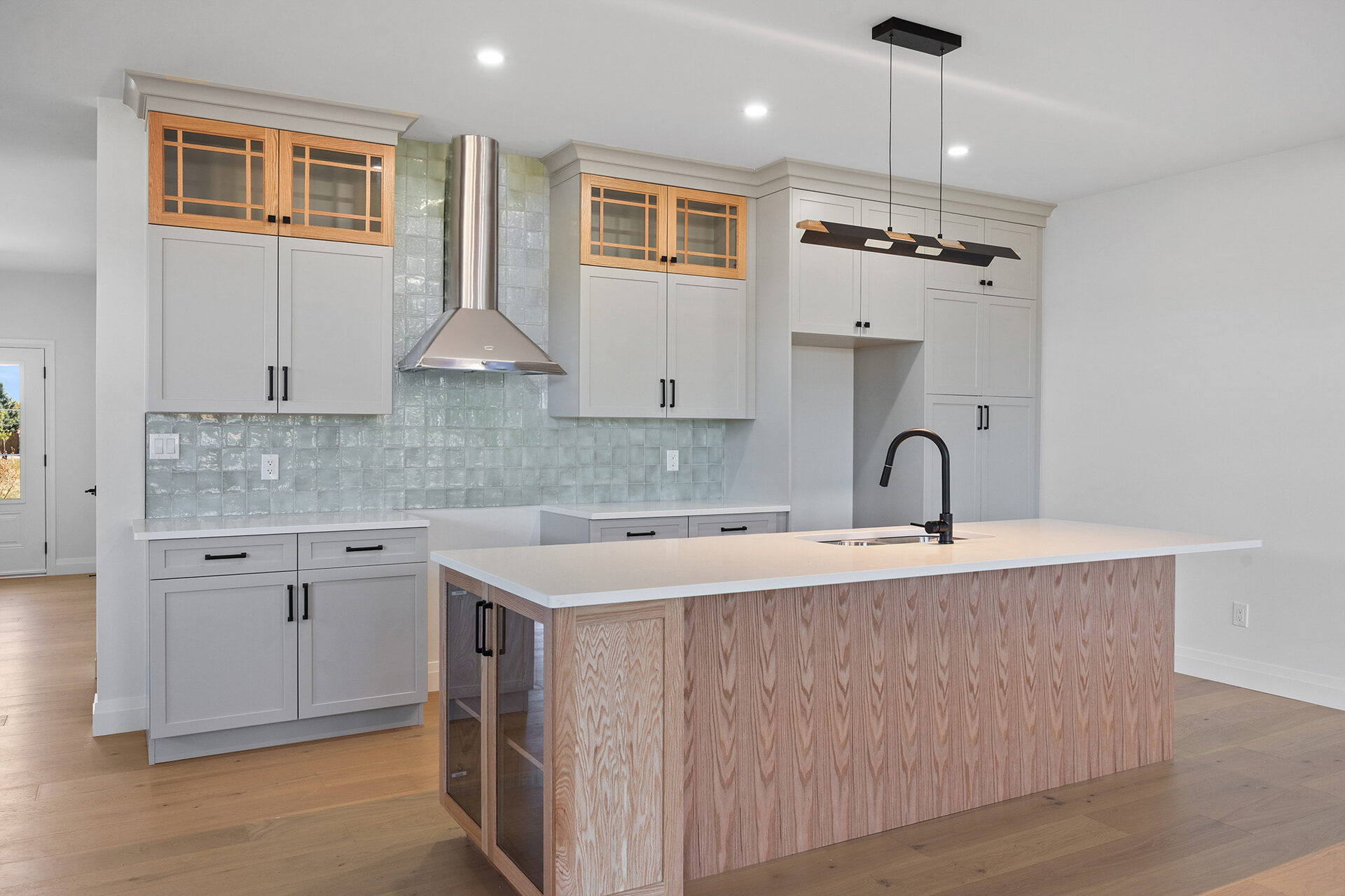 Kitchen with tiled backsplash, stainless hood and pendant lighting over the island
