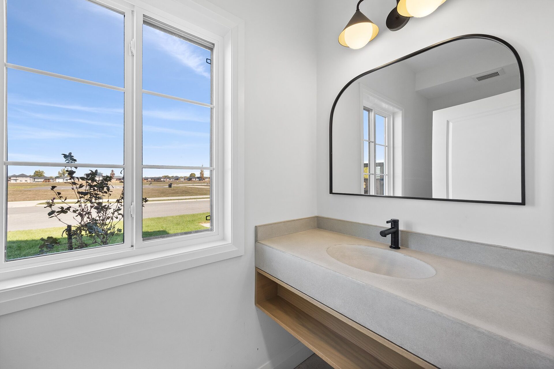 Powder room with a floating concrete vanity and an arched black-framed mirror
