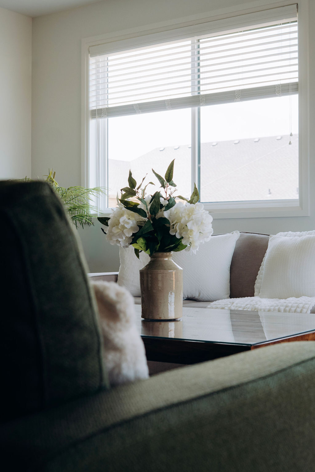 Close view of an olive armchair with a sheepskin cushion, hydrangeas and the cream sofa behind