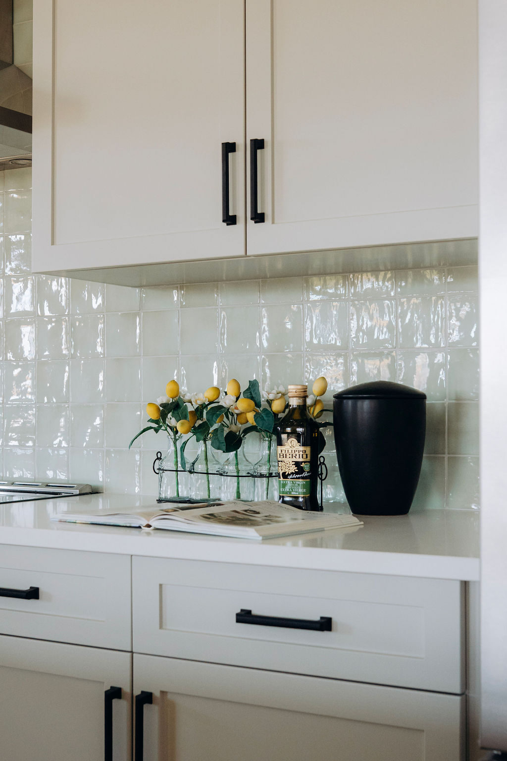 Backsplash detail, with lemons in a glass vase and olive oil set against the pale green tile