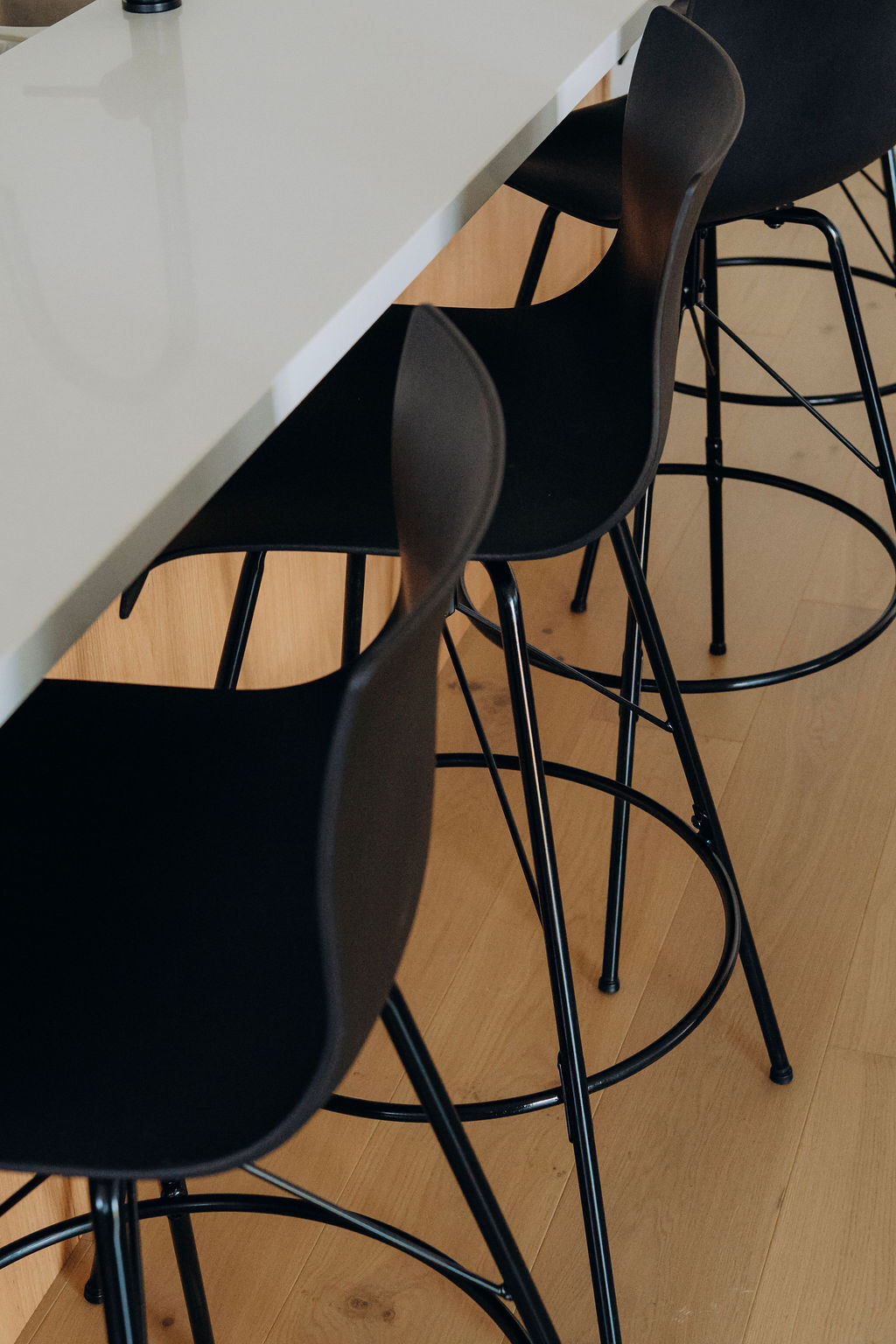 Black bar stools tucked under the quartz counter edge, above wide-plank oak flooring