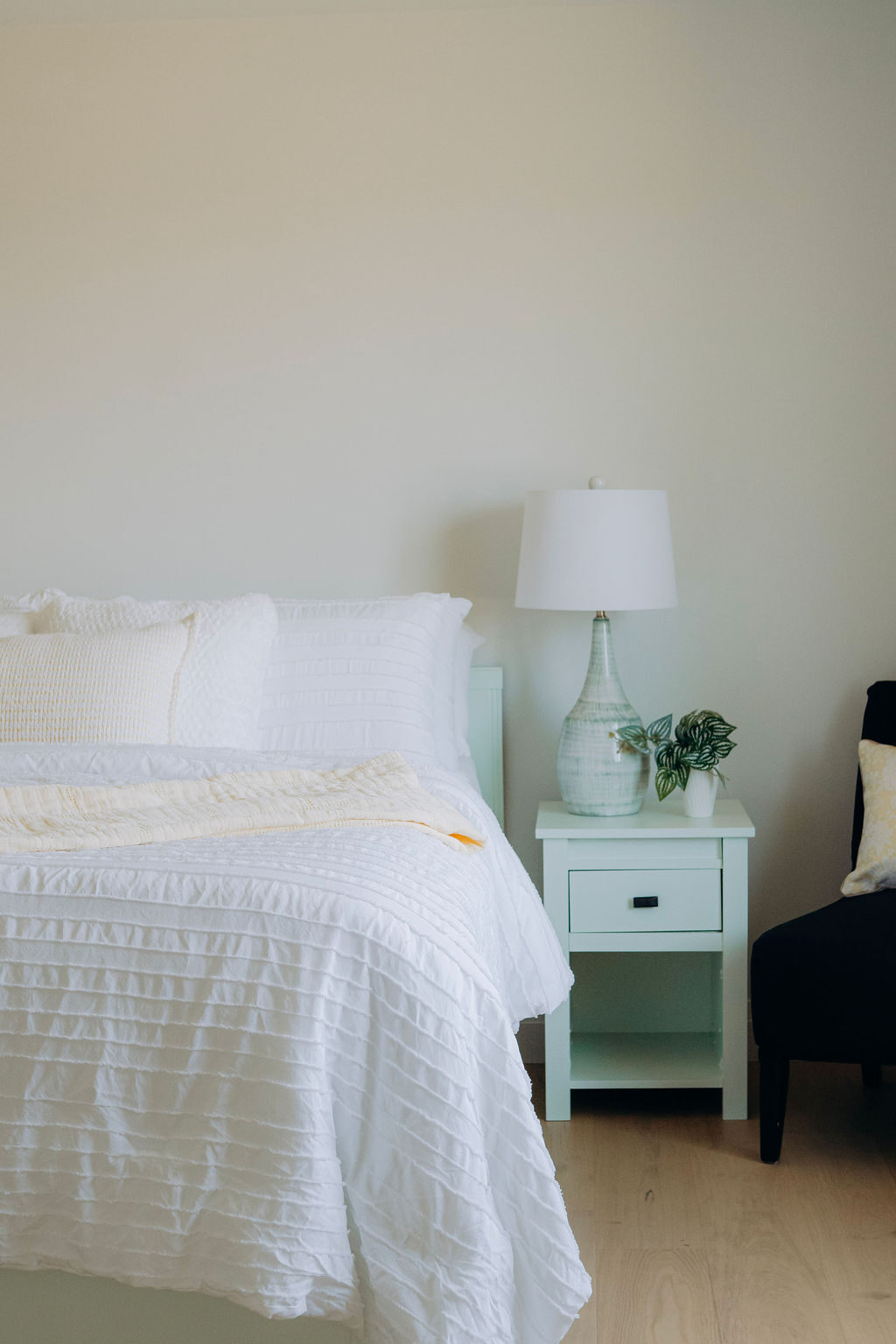 A bedroom made up in white bedding, with a pale green nightstand and a table lamp beside the bed