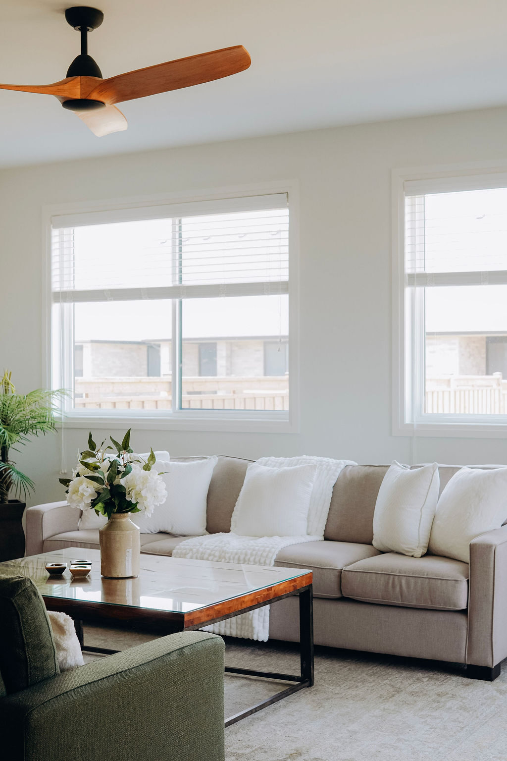 The great room of the model home seen across the coffee table, with the cream sectional and olive armchairs beneath the windows