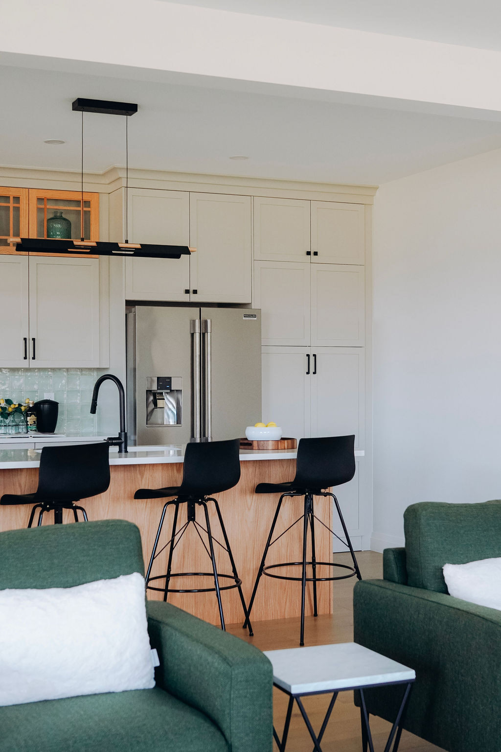 The model home kitchen island and stools seen past the green upholstered seating of the great room