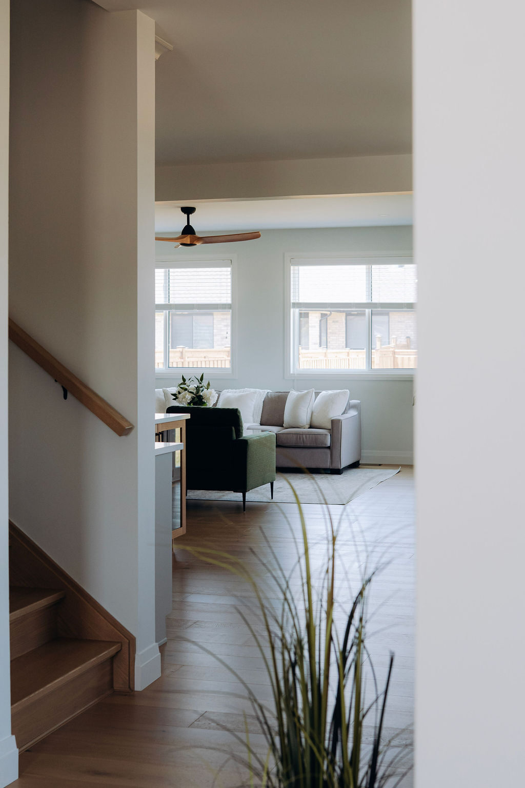 View from the stair landing down into the great room, with the ceiling fan and windows beyond