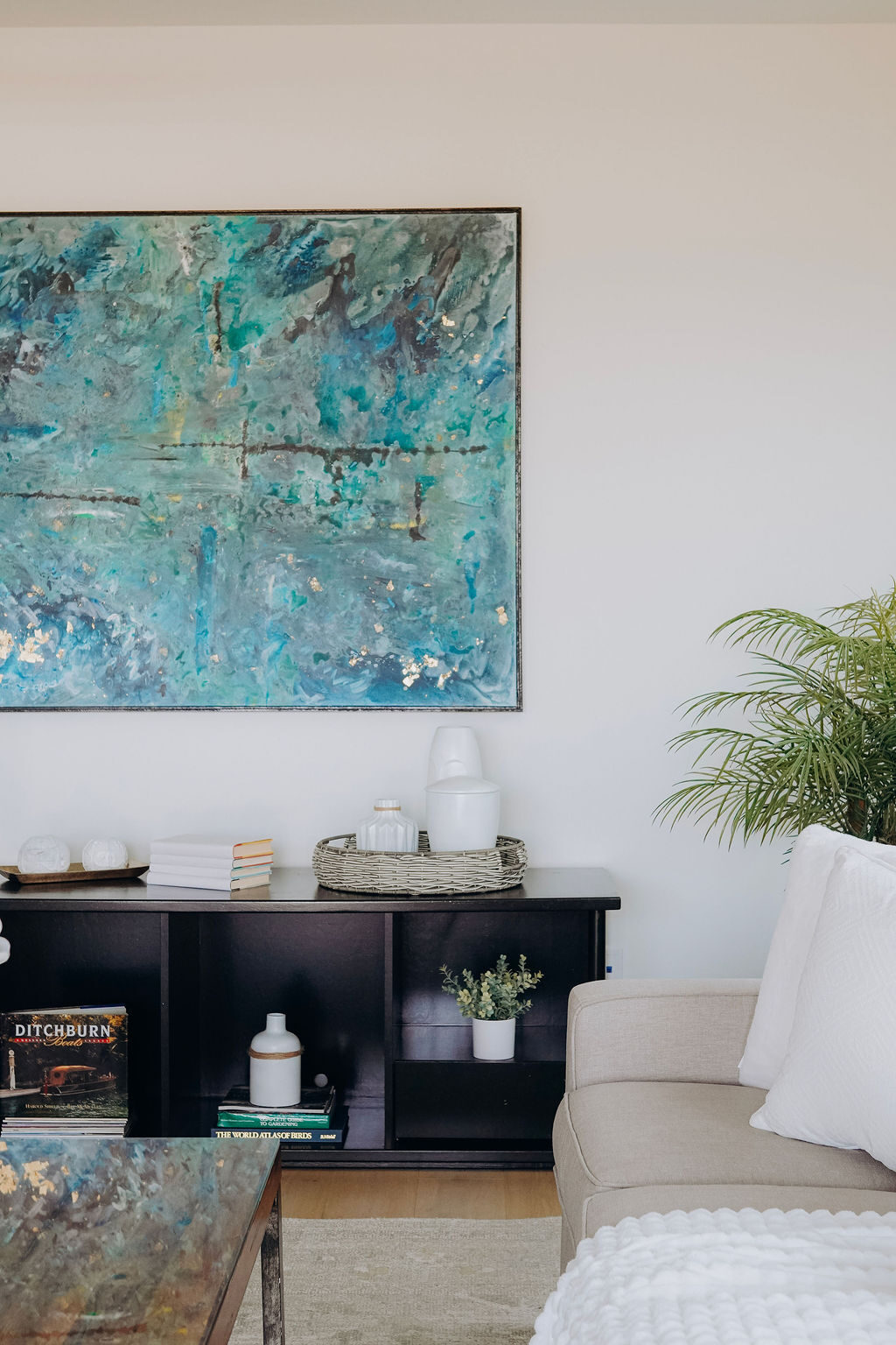 Living room corner with the teal canvas above a styled console, a potted palm and a cream sofa