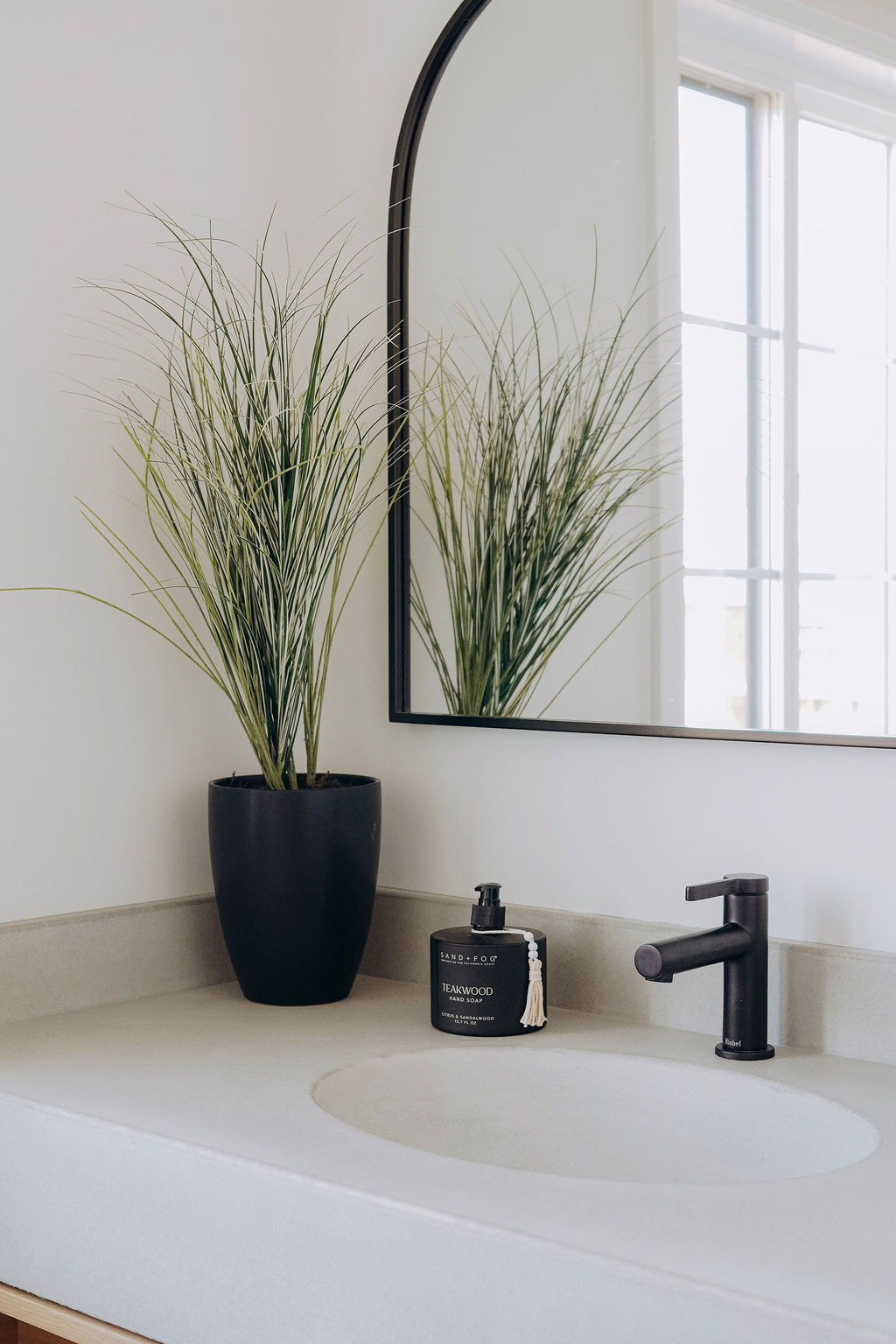 Powder room with an integrated oval basin, a black faucet and an arched black-framed mirror above
