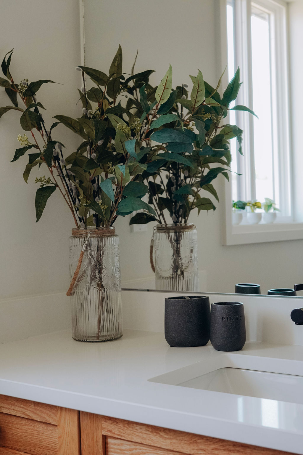 Vanity detail, with eucalyptus stems in fluted glass vases beside dark stoneware tumblers